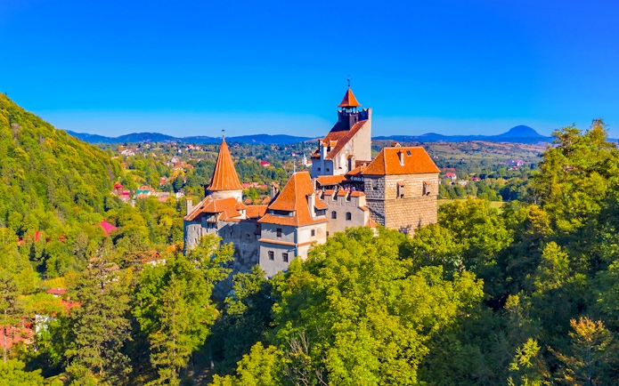Bran Castle in Romania surrounded by lush greenery and distant hills.