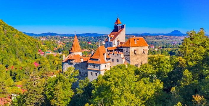 Bran Castle in Romania surrounded by lush greenery and distant hills.