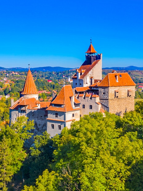 Bran Castle in Romania surrounded by lush greenery and distant hills.