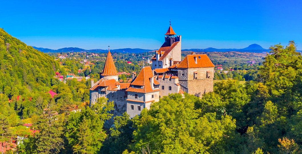Bran Castle in Romania surrounded by lush greenery and distant hills.