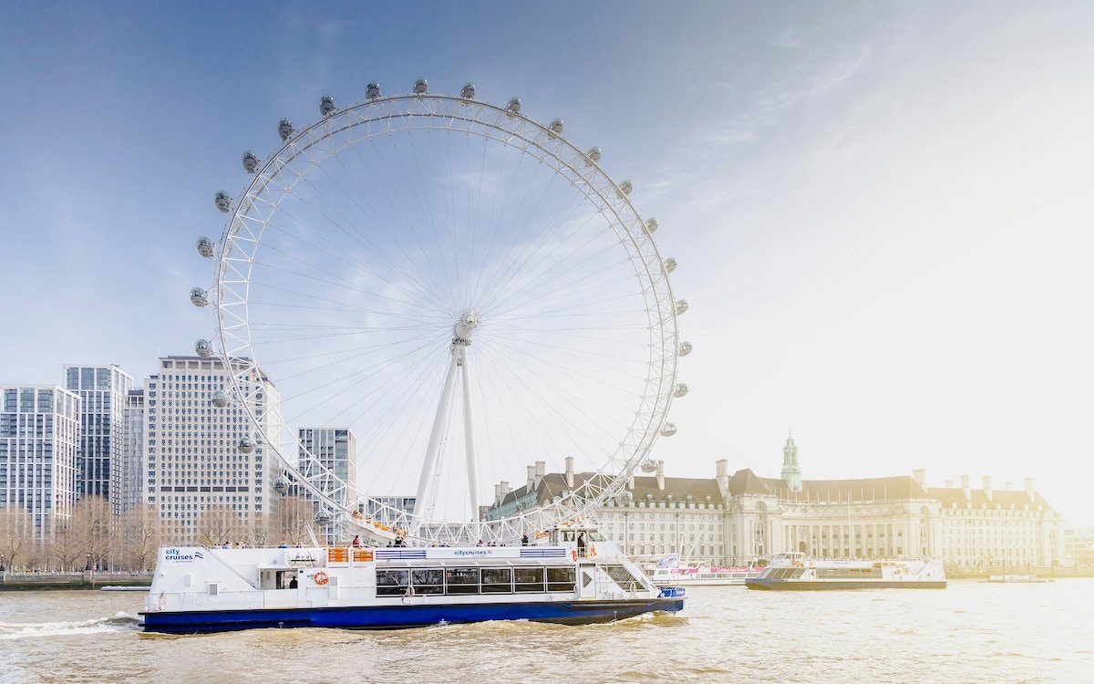 Thames River cruise boat passing by the London Eye in London, UK.