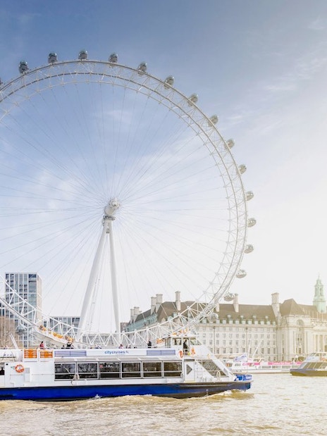 Thames River cruise boat passing by the London Eye in London, UK.