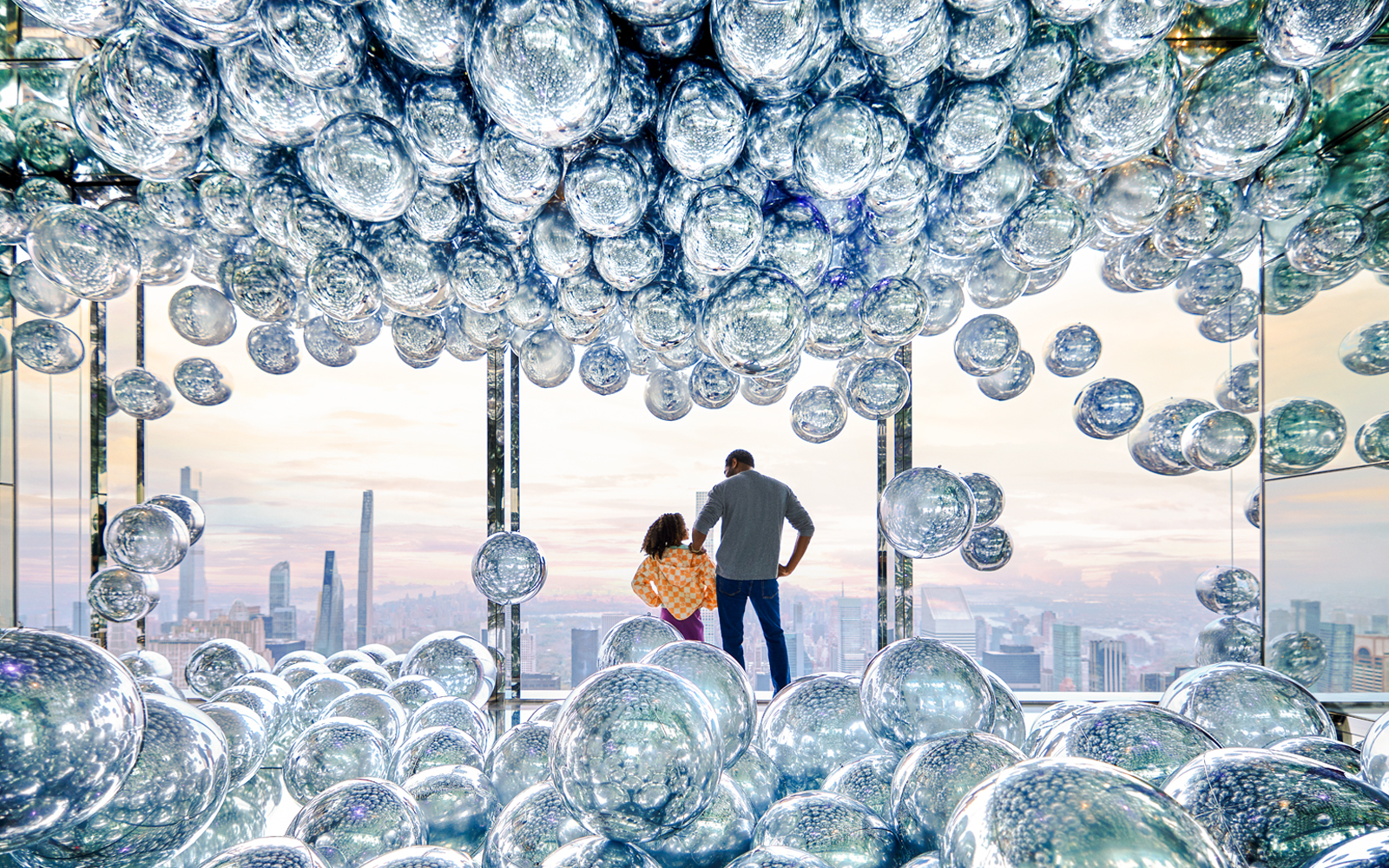 Visitors at SUMMIT One Vanderbilt observation deck with reflective spheres, New York City skyline in view.