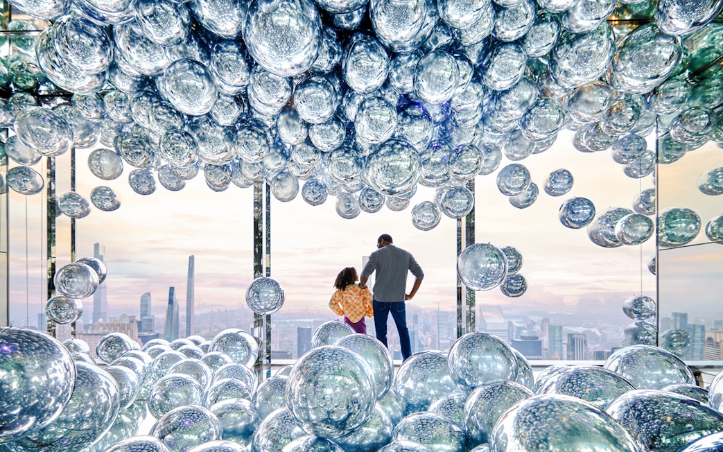 Visitors at SUMMIT One Vanderbilt observation deck with reflective spheres, New York City skyline in view.