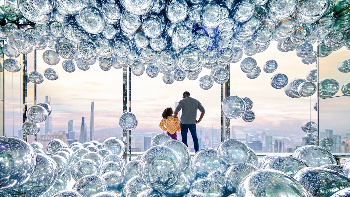 Visitors at SUMMIT One Vanderbilt observation deck with reflective spheres, New York City skyline in view.