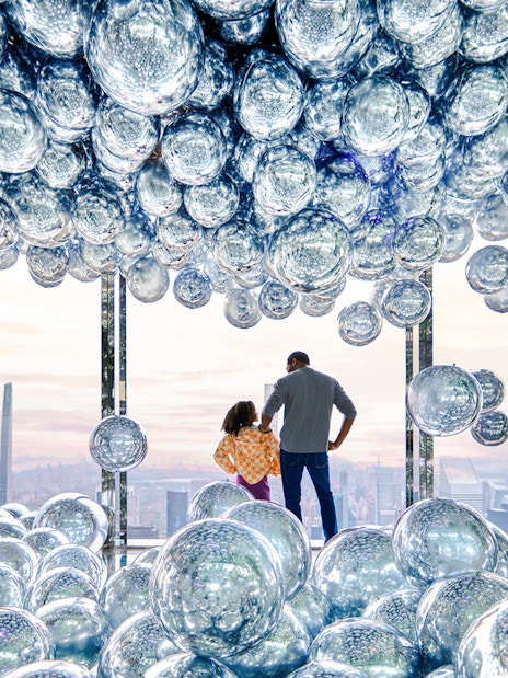 Visitors at SUMMIT One Vanderbilt observation deck with reflective spheres, New York City skyline in view.