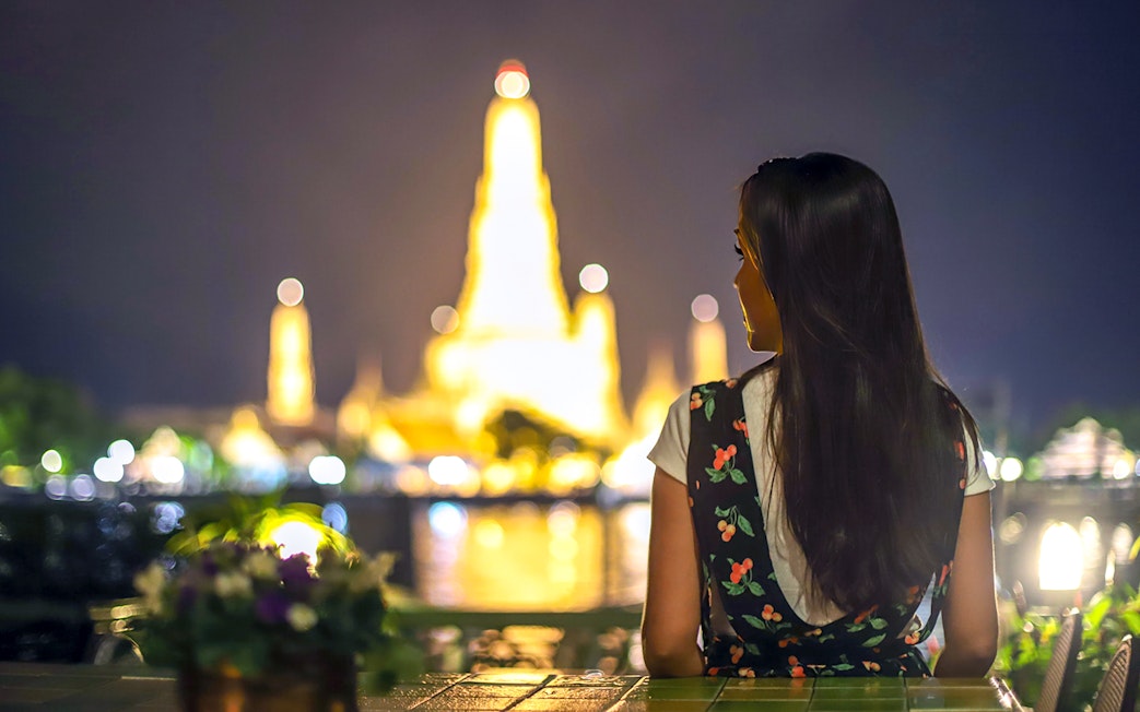Woman viewing illuminated Wat Arun at night, Bangkok Night Tour.