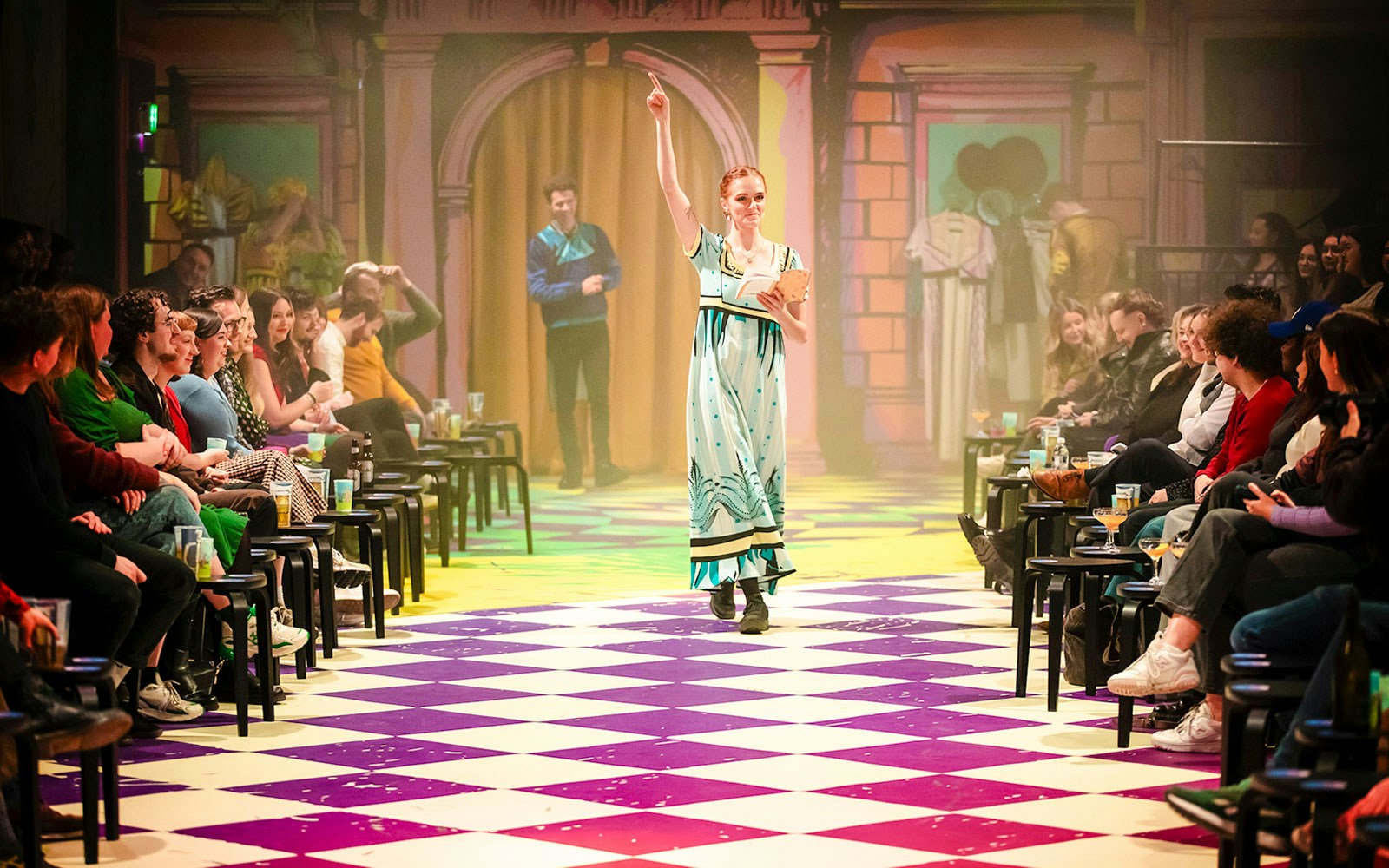 Audience watching a performer in a colorful theater setting during Plied and Prejudice show.