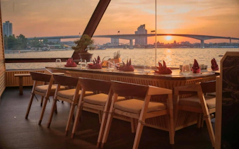 Dining table set for Okura Cruise Bangkok with sunset view over the river.