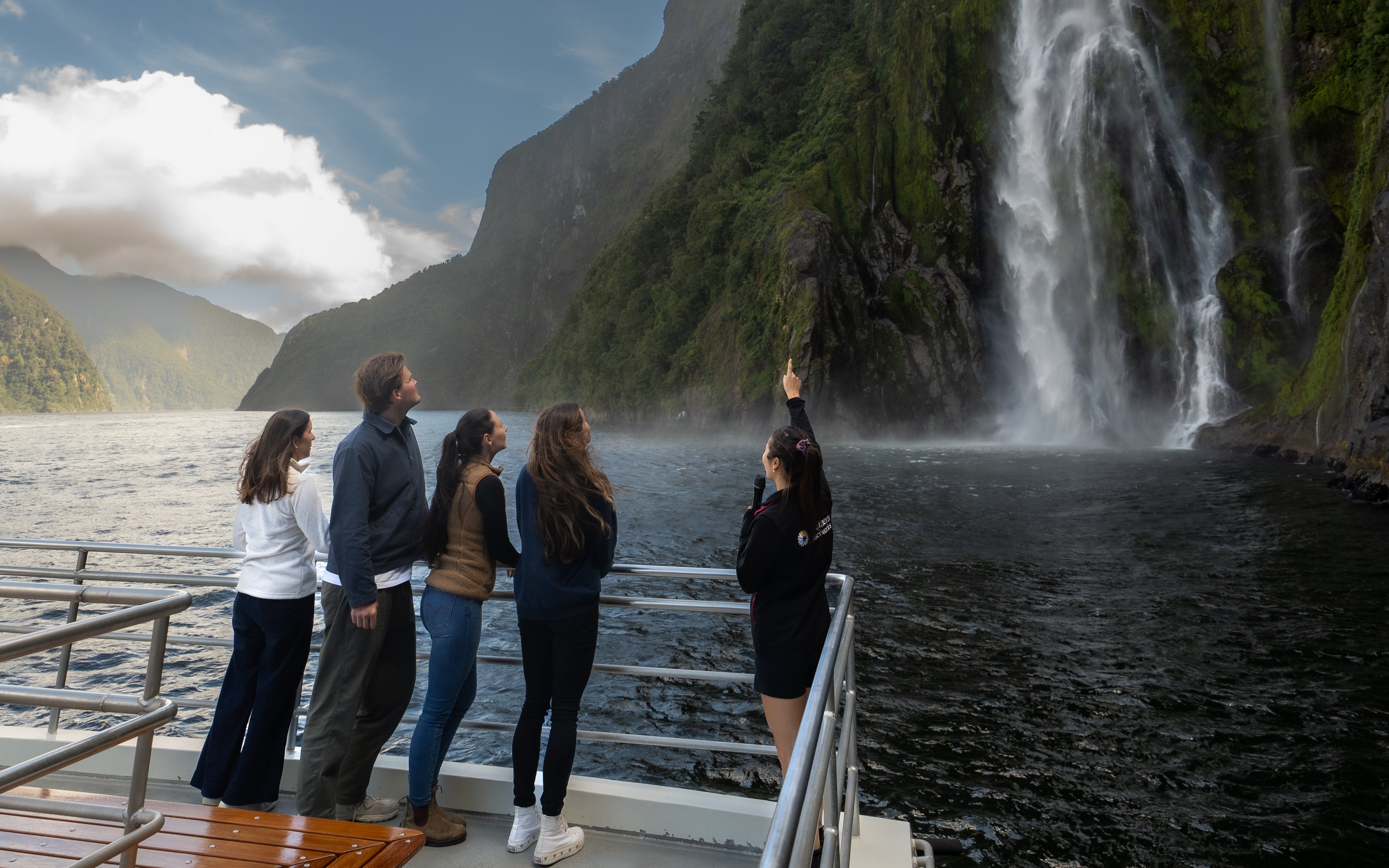 Tourists on a boat admire a waterfall at Milford Sound, New Zealand.