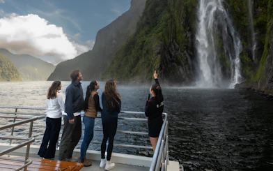 Tourists on a boat admire a waterfall at Milford Sound, New Zealand.