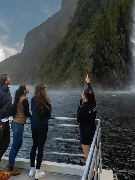 Tourists on a boat admire a waterfall at Milford Sound, New Zealand.
