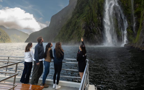 Tourists on a boat admire a waterfall at Milford Sound, New Zealand.