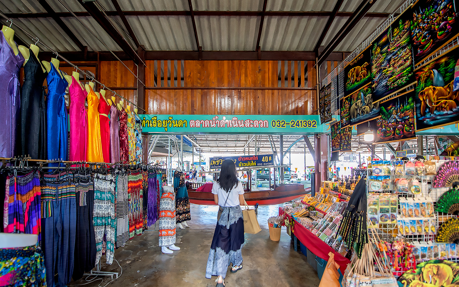 Visitor exploring colorful clothing and souvenirs at Damnoen Saduak Floating Market, Thailand.