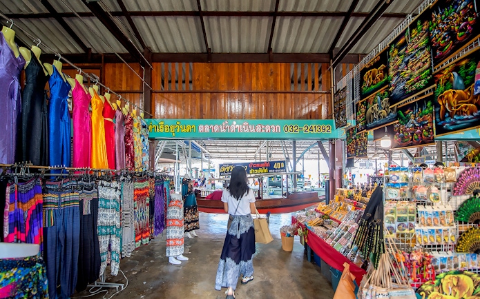 Visitor exploring colorful clothing and souvenirs at Damnoen Saduak Floating Market, Thailand.