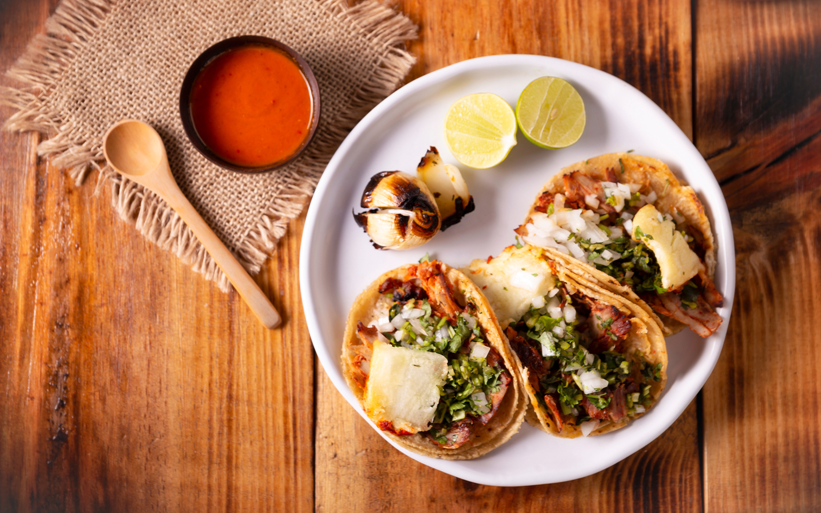 Tacos El Pastor with grilled onions, lime, and salsa on a wooden table.