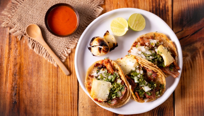Tacos El Pastor with grilled onions, lime, and salsa on a wooden table.
