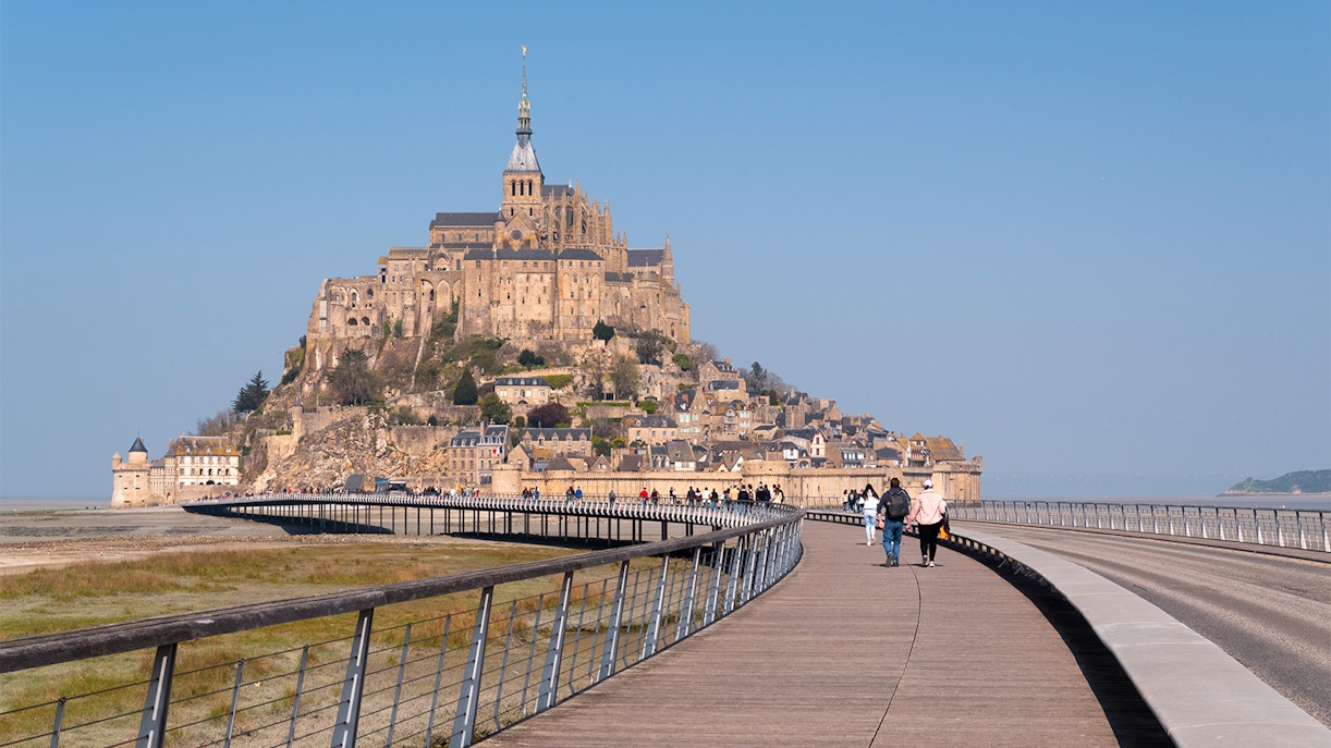 Walkway leading to Mont Saint Michel in France, with visitors approaching the historic abbey.