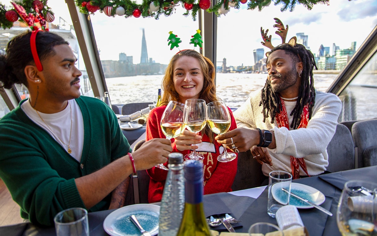 Friends toasting with wine on a Thames River Christmas lunch cruise in London.