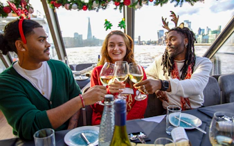 Friends toasting with wine on a Thames River Christmas lunch cruise in London.