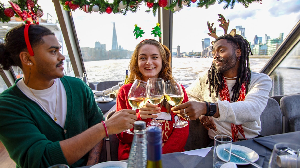 Friends toasting with wine on a Thames River Christmas lunch cruise in London.