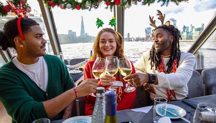 Friends toasting with wine on a Thames River Christmas lunch cruise in London.