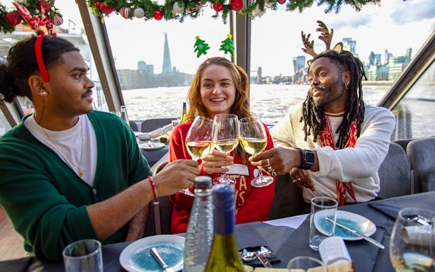 Friends toasting with wine on a Thames River Christmas lunch cruise in London.