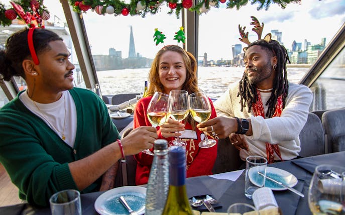Friends toasting with wine on a Thames River Christmas lunch cruise in London.