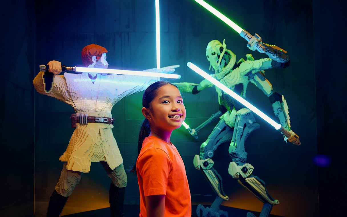 Child smiling near LEGO Star Wars lightsaber battle display at LEGOStarWarsTheExhibition.