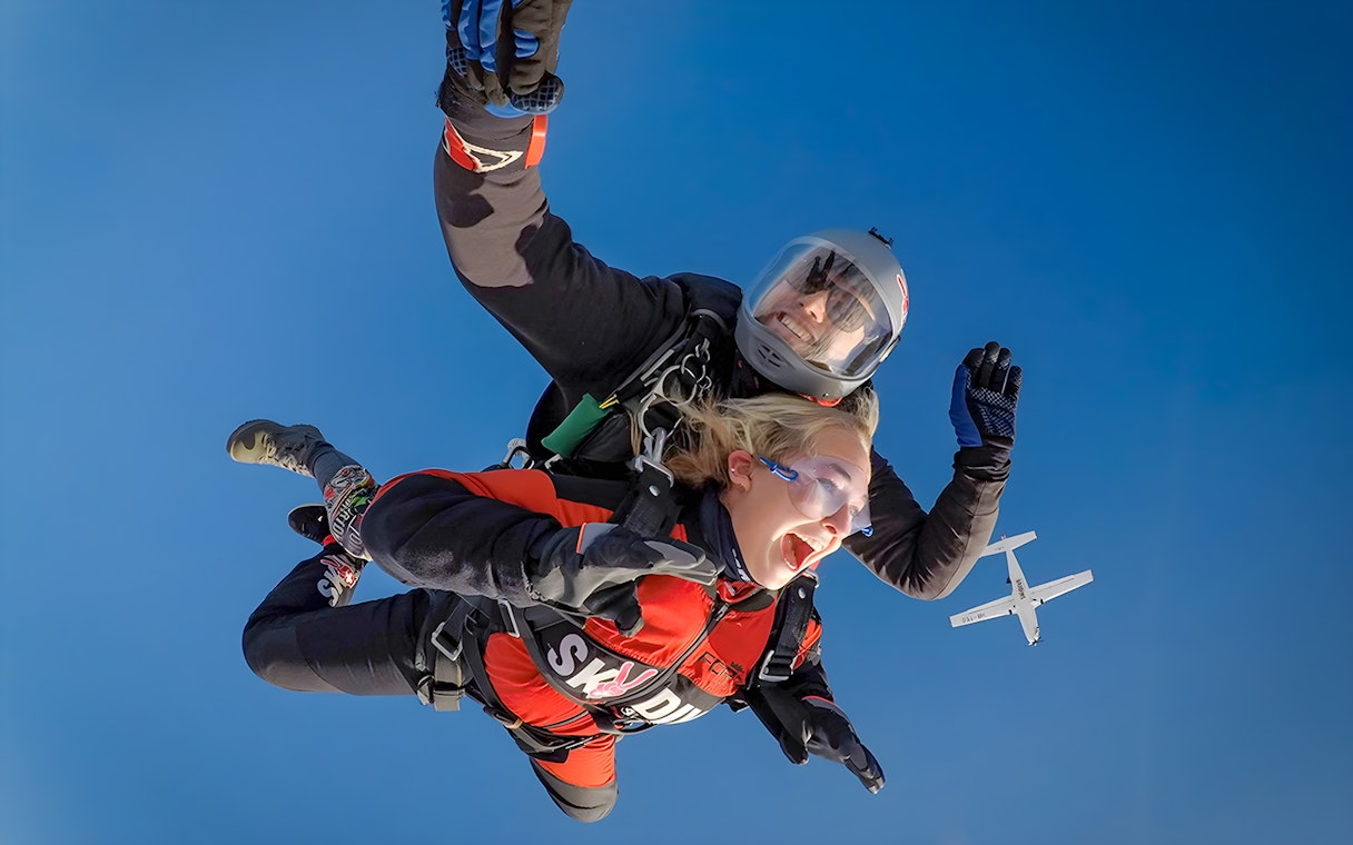 Tandem skydive over Switzerland from 13,000 ft with plane in background.