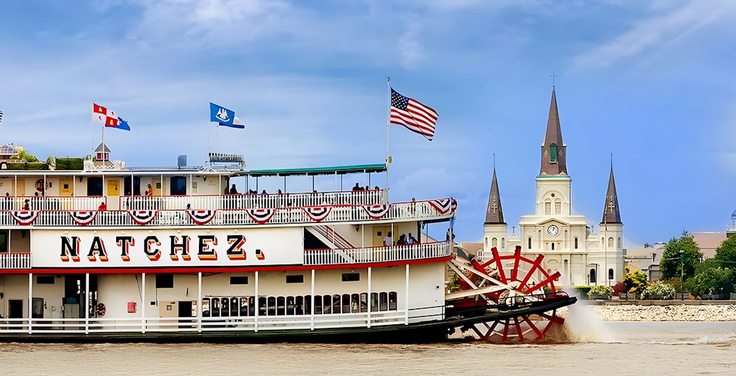 Steamboat Natchez sailing on the Mississippi River with the city in the background.