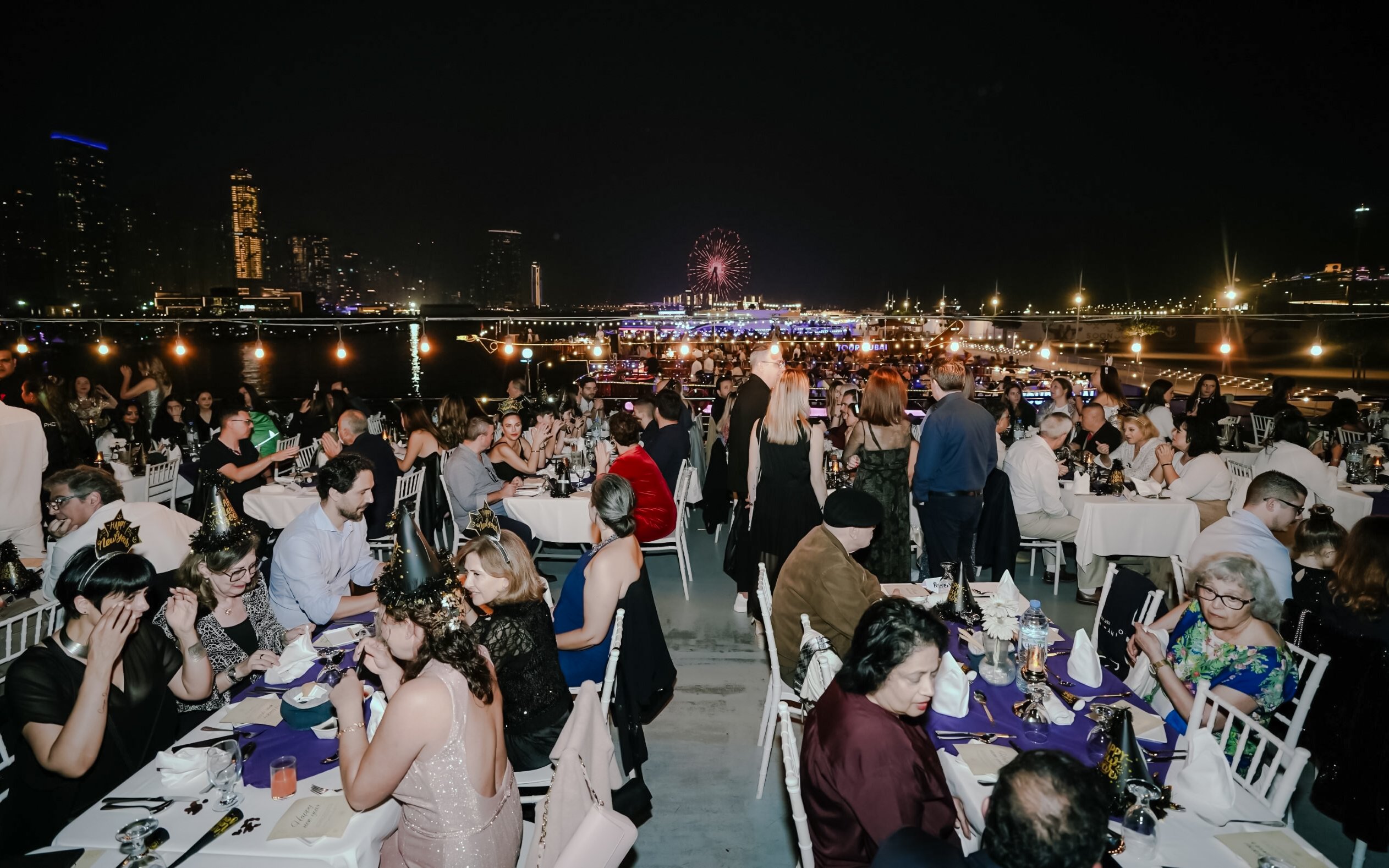 Guests dining on a New Year's Eve Marina Dhow Dinner Cruise with city skyline and fireworks.