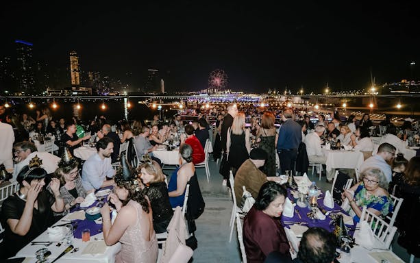 Guests dining on a New Year's Eve Marina Dhow Dinner Cruise with city skyline and fireworks.