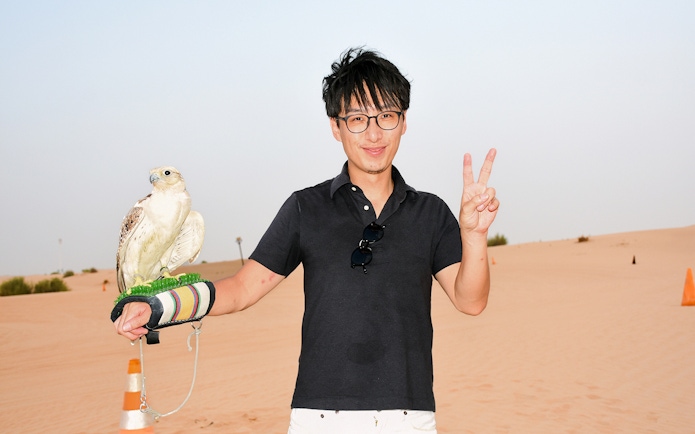 Man holding a falcon in a desert setting.