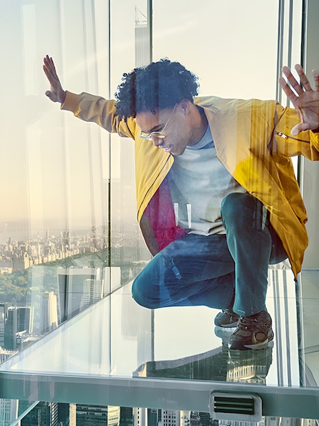 Man crouching on glass floor with view of New York City skyline at SUMMIT OV.