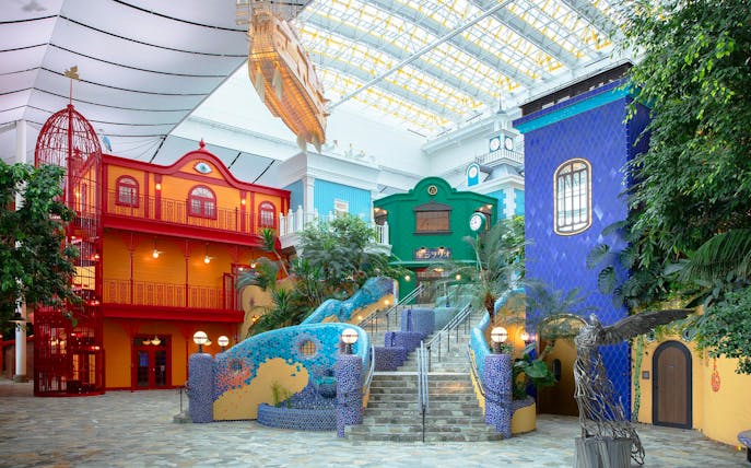 Ghibli's Grand Warehouse colorful buildings and staircase with lush greenery.