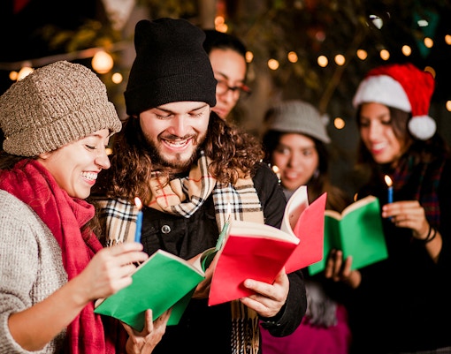 Group singing Christmas carols at Prague Castle with festive lights.