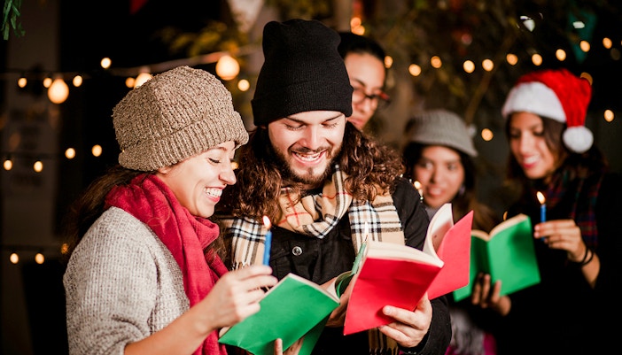 Group singing Christmas carols at Prague Castle with festive lights.
