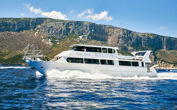 Deluxe boat cruising La Maddalena Archipelago with rocky cliffs in the background.
