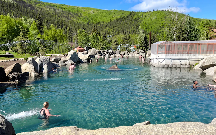 Visitors enjoying the natural hot springs at Chena Hot Springs Resort, surrounded by lush greenery.