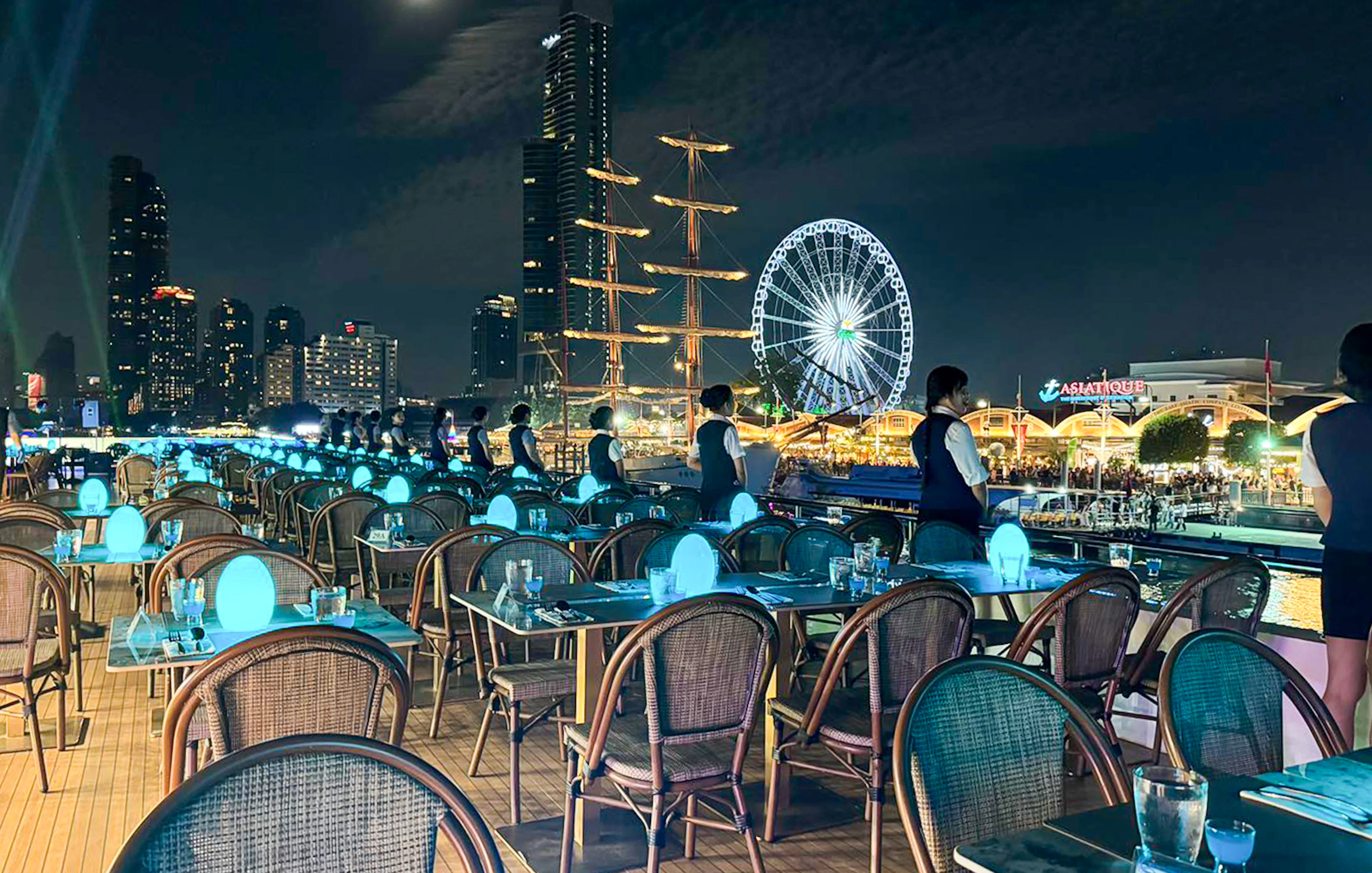 Staff preparing tables on Royal Princess cruise with Asiatique Ferris wheel in background.