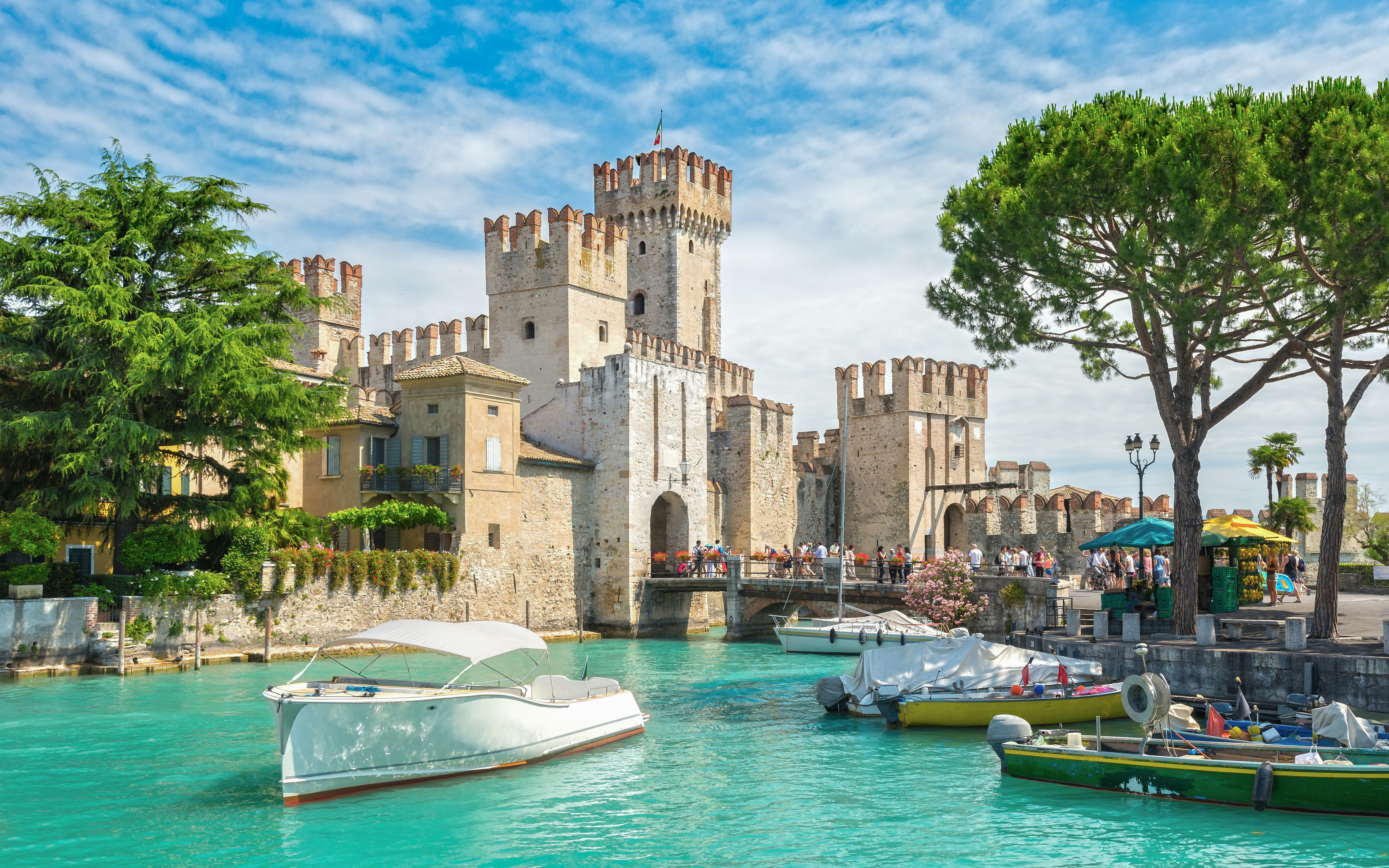 Castel Scaligero in Sirmione with boats on turquoise water and tourists exploring the area.