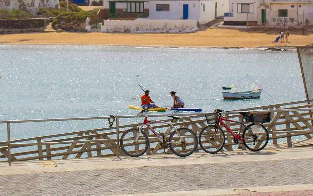 Kayakers near a pier with parked bicycles in Caleta del Sebo, La Graciosa, Canary Islands.