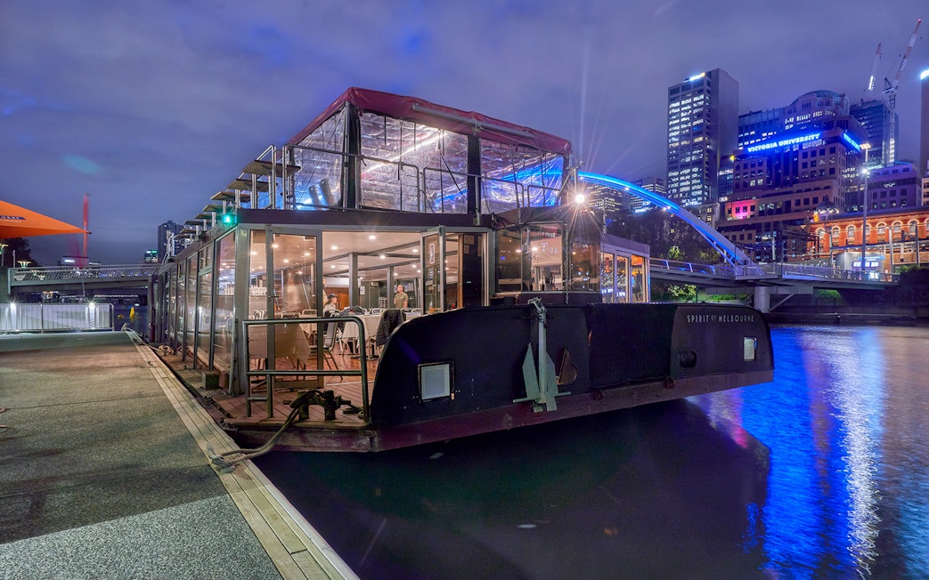 Dinner cruise boat docked on Yarra River, Melbourne, with city skyline in the background.