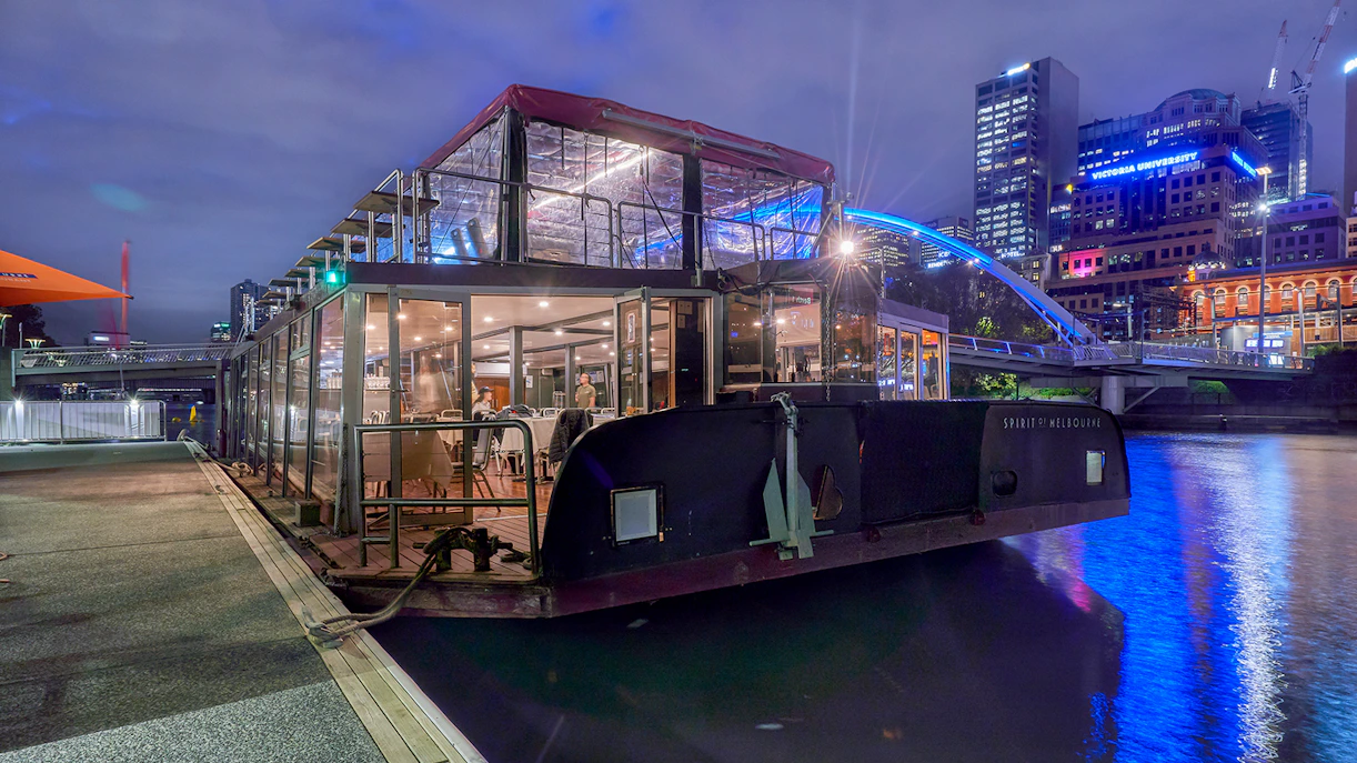 Dinner cruise boat docked on Yarra River, Melbourne, with city skyline in the background.