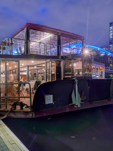 Dinner cruise boat docked on Yarra River, Melbourne, with city skyline in the background.