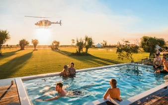 Helicopter flying over guests in a pool at Top End Safari Camp, Finniss River.