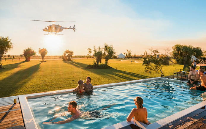 Helicopter flying over guests in a pool at Top End Safari Camp, Finniss River.