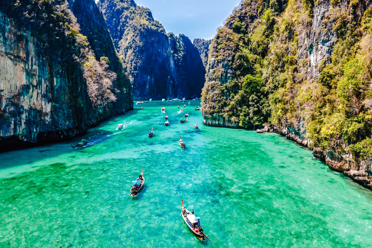 Boats navigating turquoise waters between limestone cliffs, Phuket to Phi Phi ferry route.
