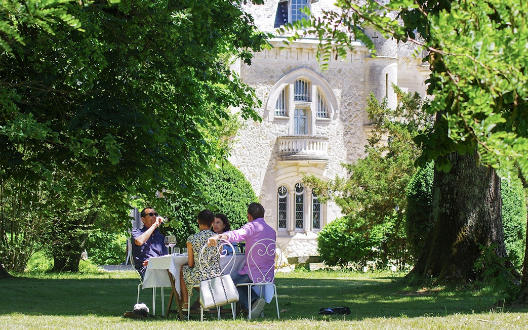 Group enjoying wine at a table in a garden near a historic building in Saint-Emilion.